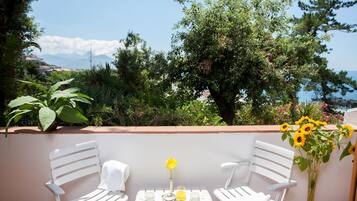 A terrace with two white chairs and a table set with a flower vase, a teapot, and cups.
