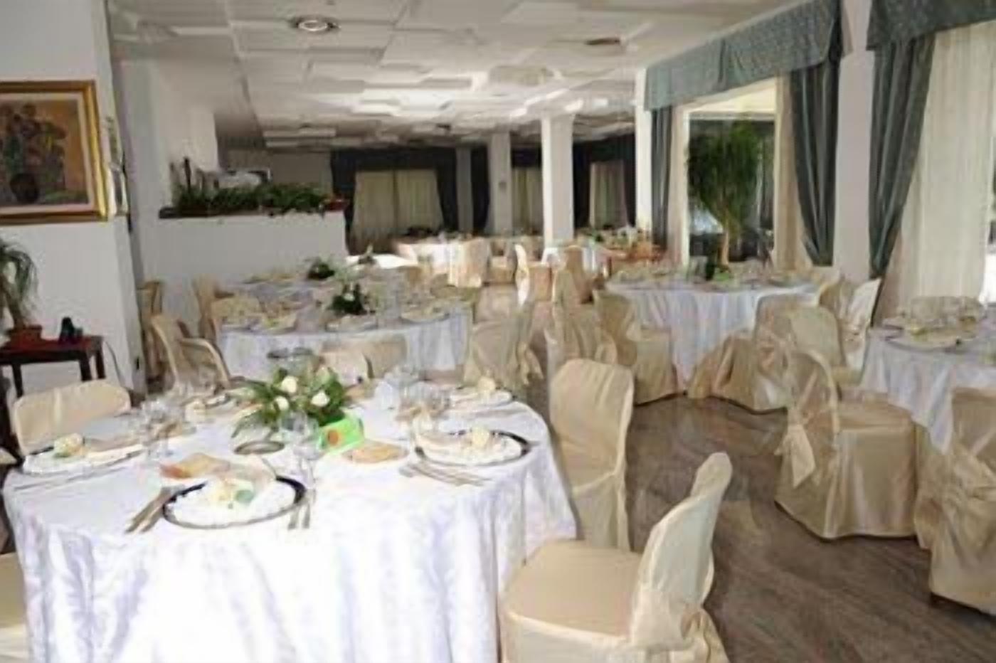 Un salón de banquetes con mesas redondas dispuestas para comer, sillas con cubres protectores color beige y mantel blanco.
