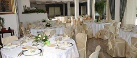 A banquet hall with round tables set for dining, chairs with beige covers, and a white tablecloth.