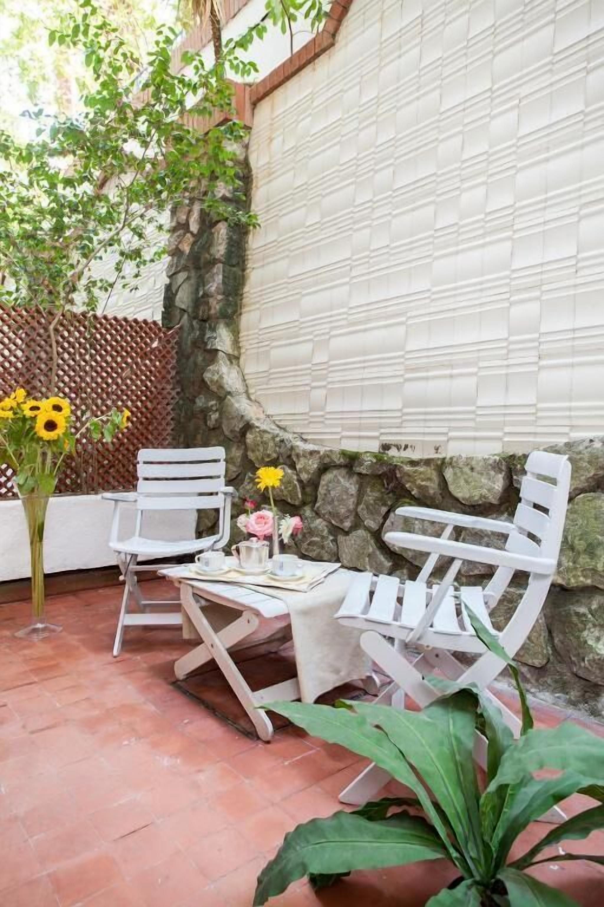 Un patio con sillas blancas, una mesa y un jarrón de flores.