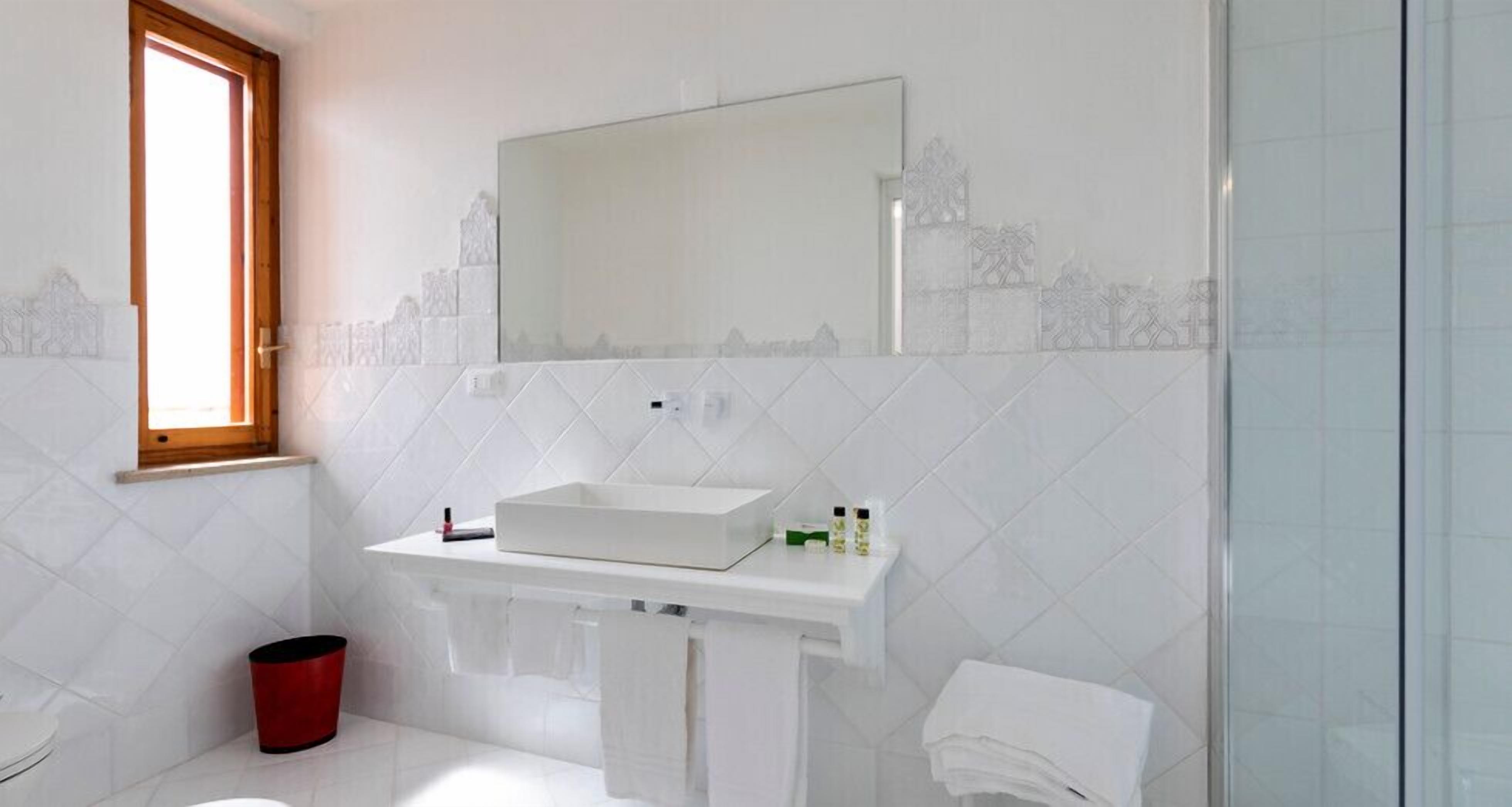 A bathroom with a white sink, a mirror, and a red trash bin.