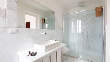 Un baño moderno con tocador blanco, un espejo grande y cabina de ducha con paredes de vidrio.