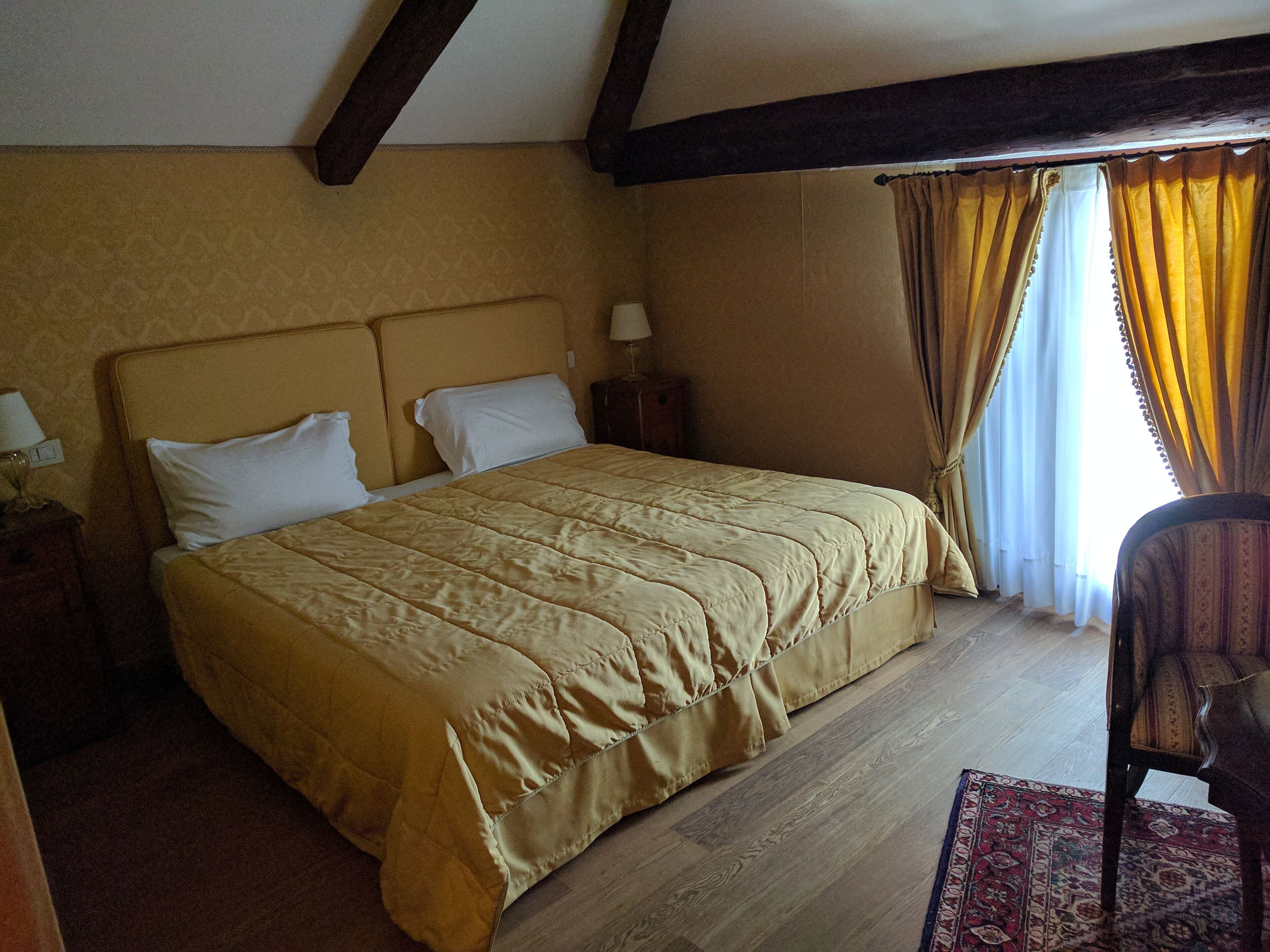 Una camera da letto con un letto grande, travi in legno al soffitto, un comodino con una lampada e una sedia.