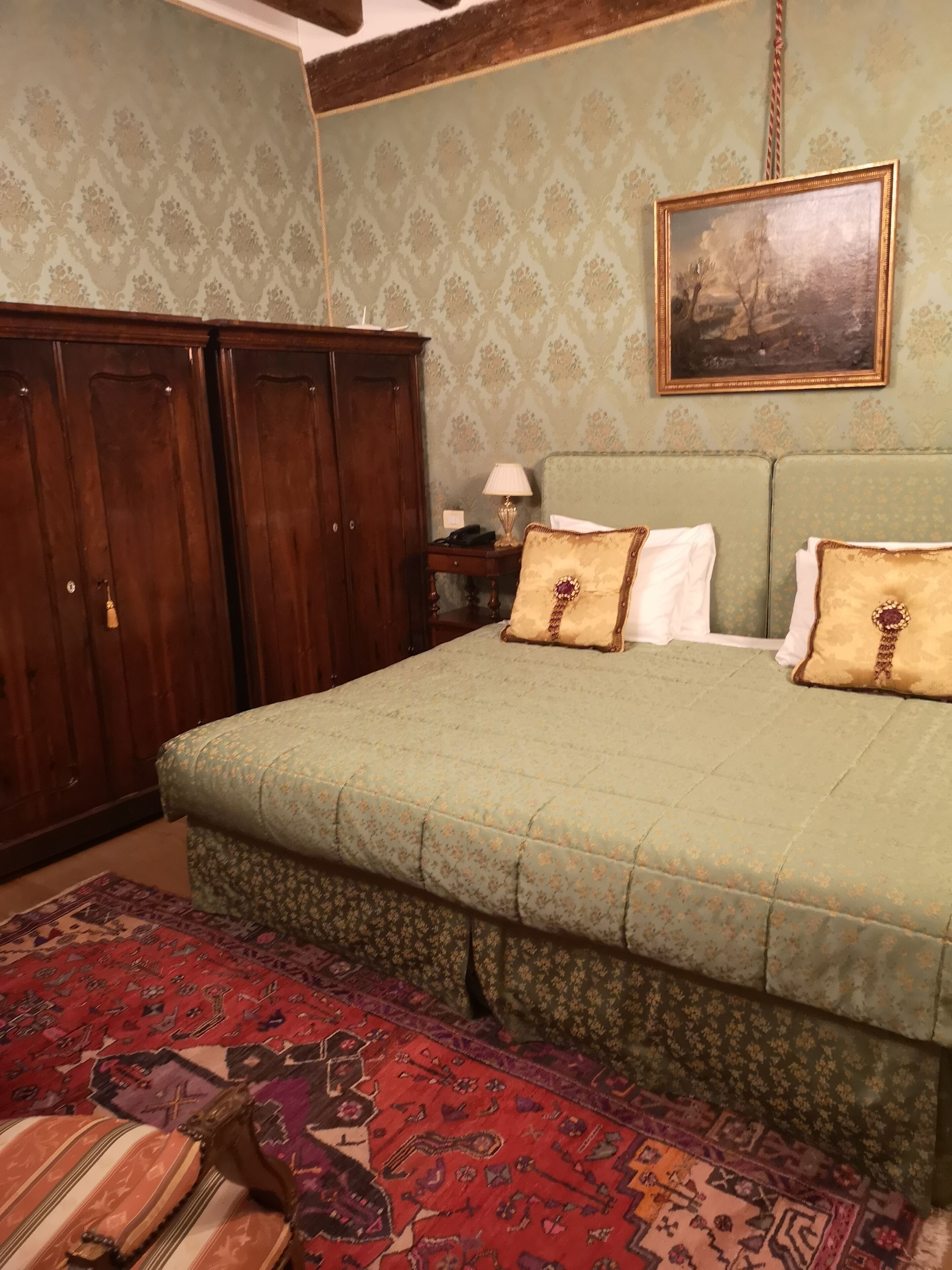 Una camera da letto con un grande letto, un armadio in legno, un tappeto decorato e un quadro appeso al muro.