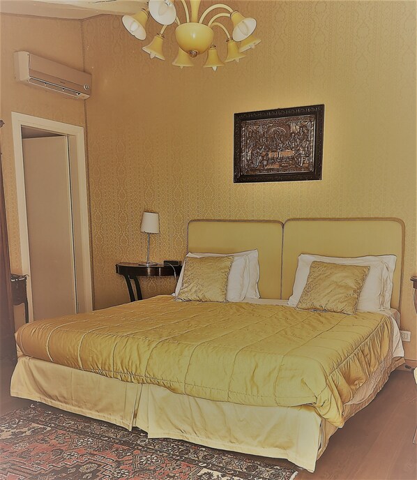 A bedroom with a bed, a nightstand, a lamp, a wall-mounted air conditioner, and a framed picture. - Relais Alberti (Venice)