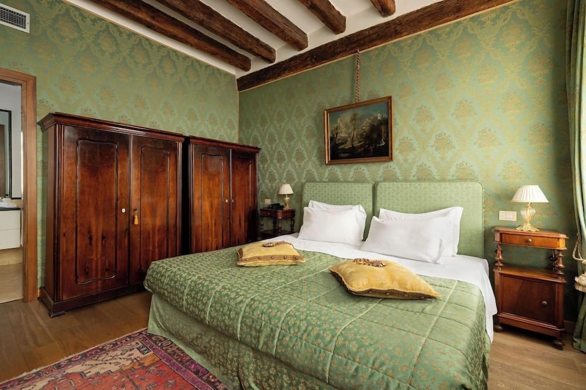 A bedroom with a large bed, wooden wardrobe, and a painting on the wall.