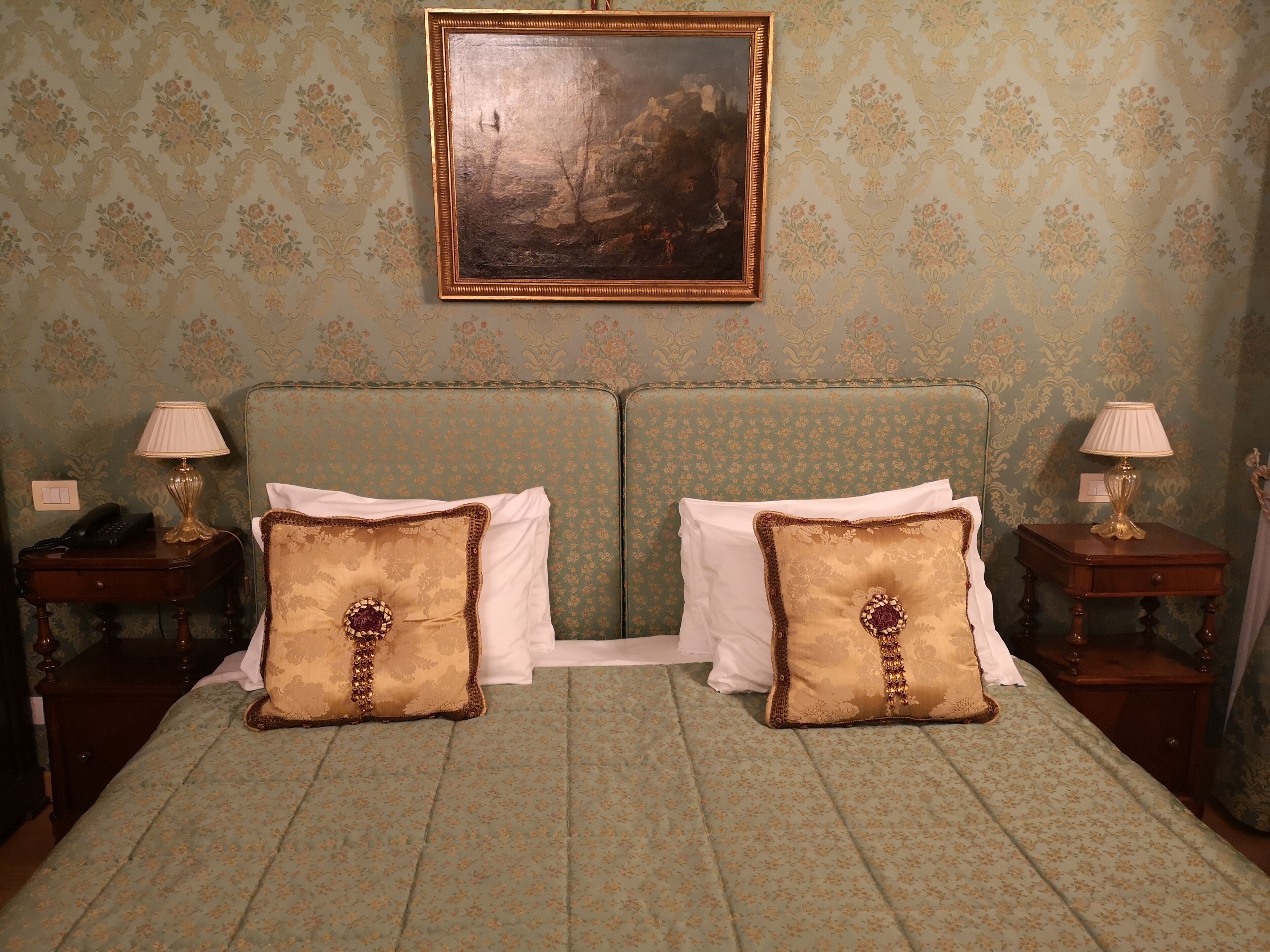 Ein Schlafzimmer mit einem grünen, gepolsterten Kopfteil, zwei Nachttischen mit Lampen und zwei Zierkissen.