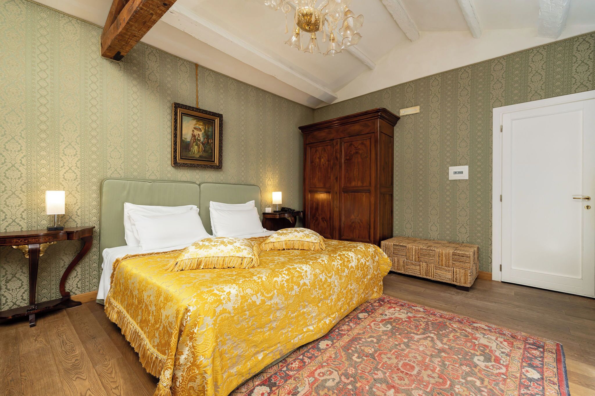 A bedroom with a large bed, a wooden wardrobe, a nightstand, and a patterned rug.