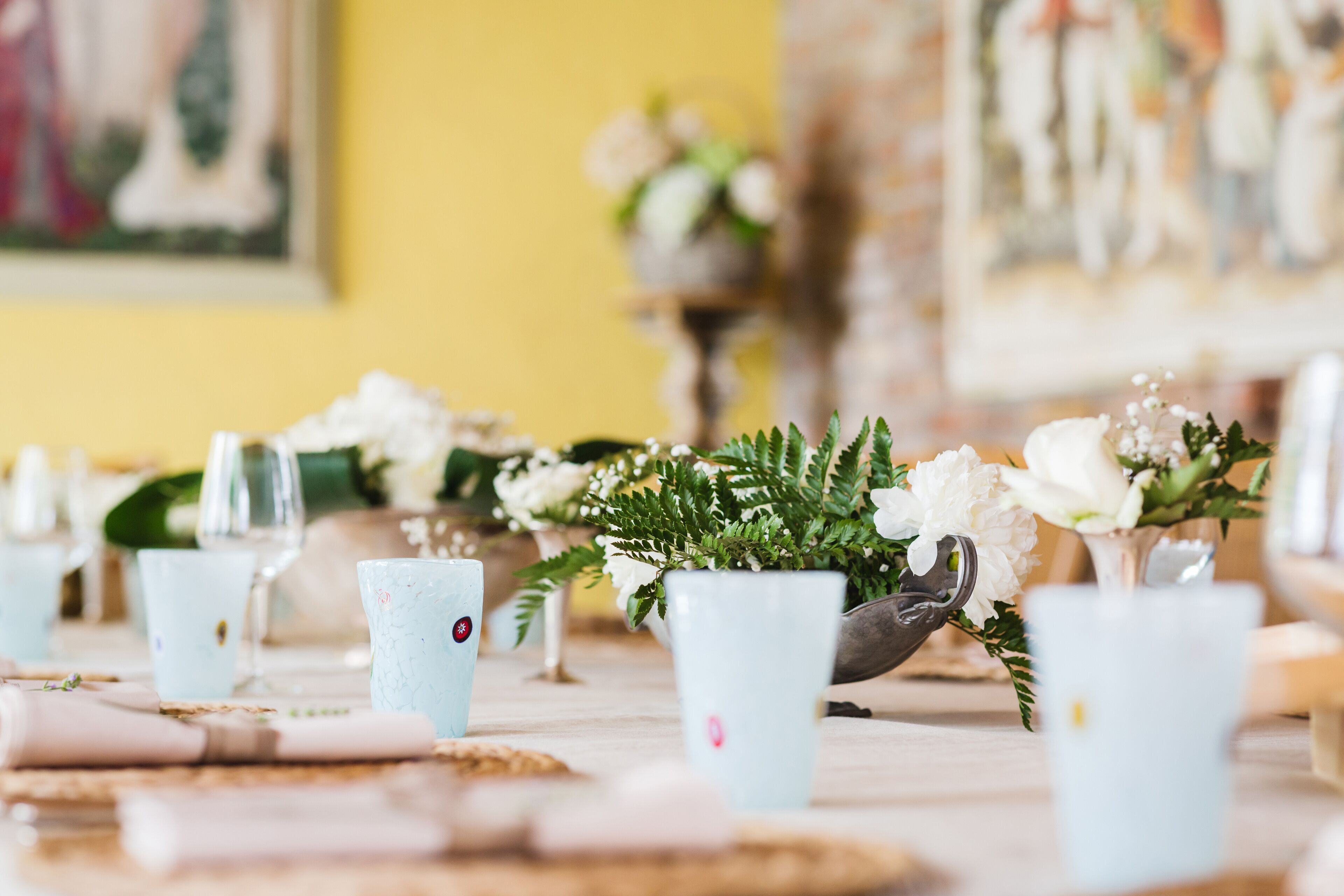 Een tafel gedekt met lichtblauwe bekers, witte bloemen en een kaars.
