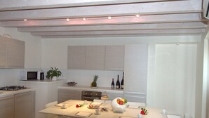 Une cuisine moderne avec des meubles blancs, une table à manger pour quatre personnes et un petit îlot central équipé d’un four à micro-ondes et d’une machine à café.