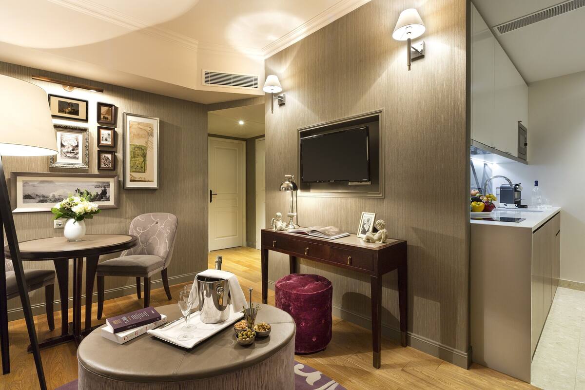 Ein modernes Hotelzimmer mit Essbereich, einem an der Wand befestigten Fernseher, einer kleinen Küchenzeile und einer gemütlichen Sitzecke.