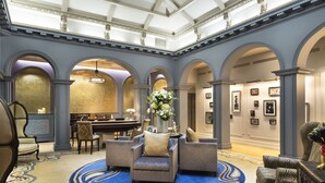 Eine geräumige Lobby mit einer imposanten Treppe, einer Sitzecke mit Sofas und Sesseln sowie einem Essbereich mit einem Klavier.