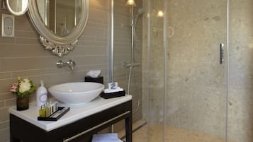 A bathroom with a large oval mirror, a white sink, and a glass-enclosed shower.