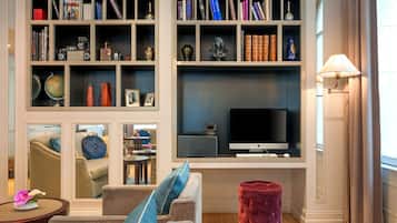 A living room with a sofa, a red ottoman, a bookshelf, a flat-screen TV, and a lamp.