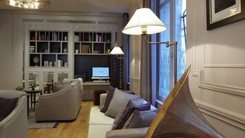 A spacious living room with a high ceiling, a grand piano, a television, and a bookshelf filled with books.