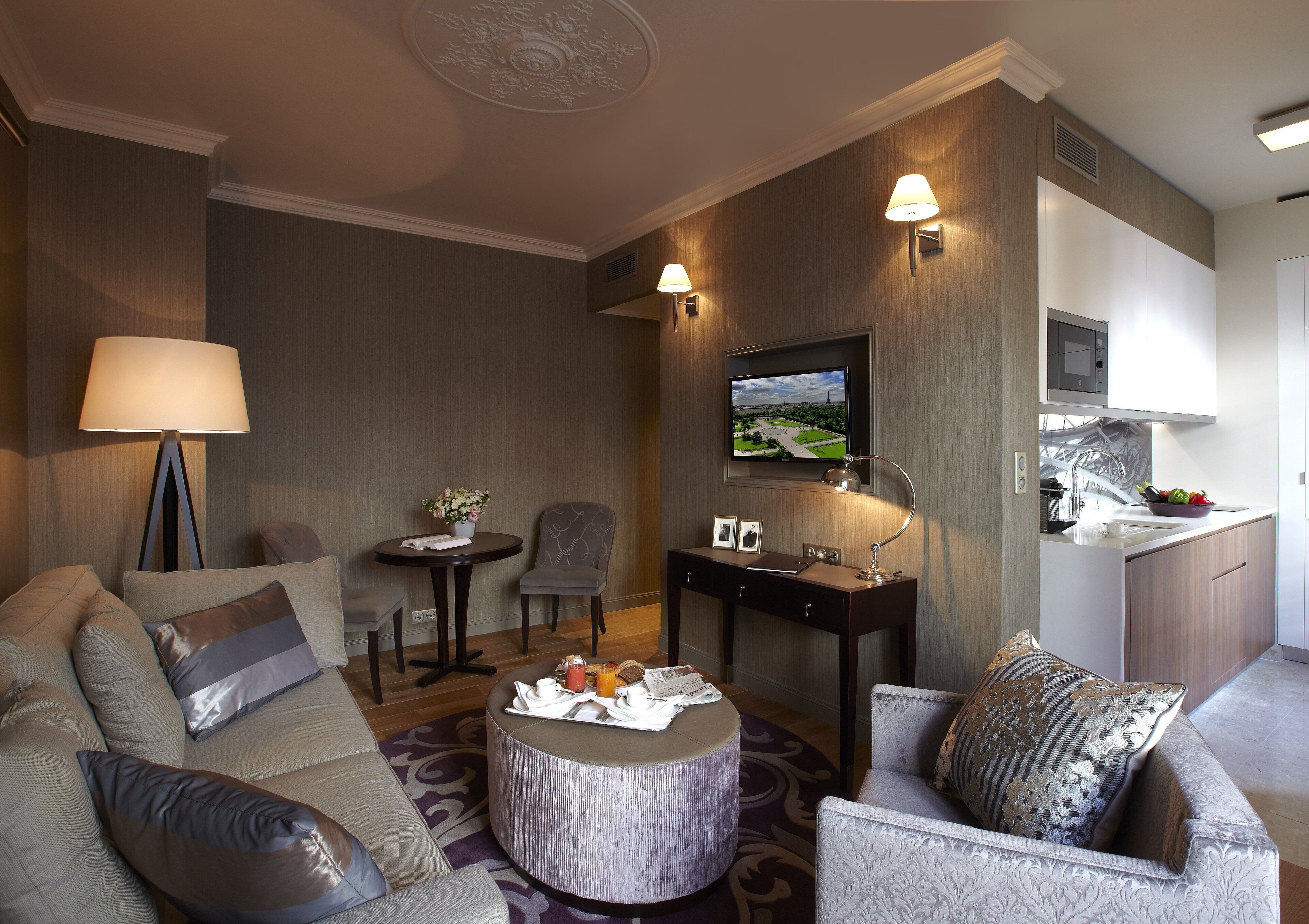Una habitación de hotel moderna con sofá, sillón, una mesita redonda y una pequeña zona de comedor con mesa y sillas.