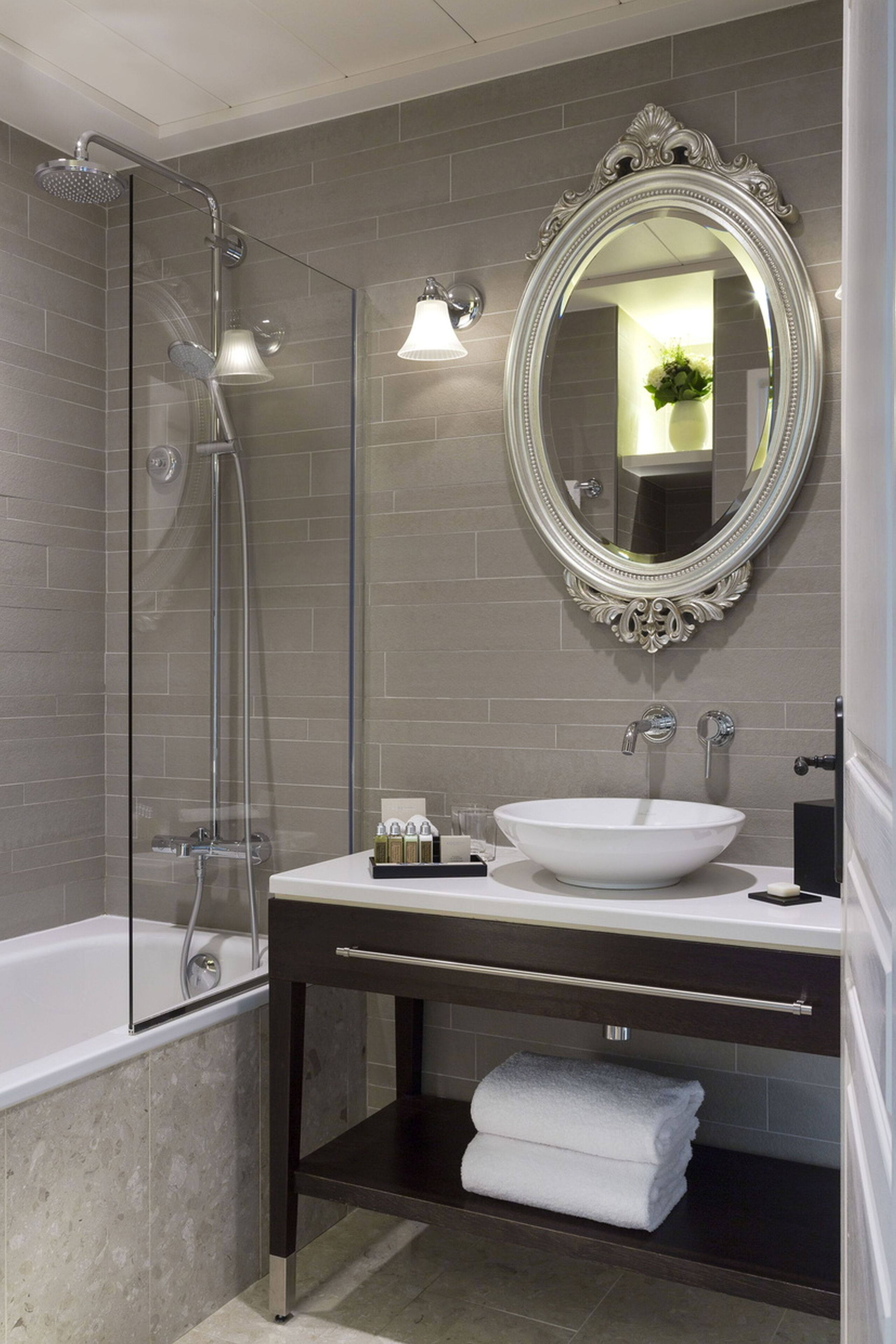 A modern bathroom with a glass-enclosed shower, a white sink, and a large ornate mirror.