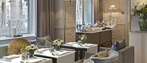 A dining area with tables set for a meal, cushioned seating, and a decorative vase with flowers.