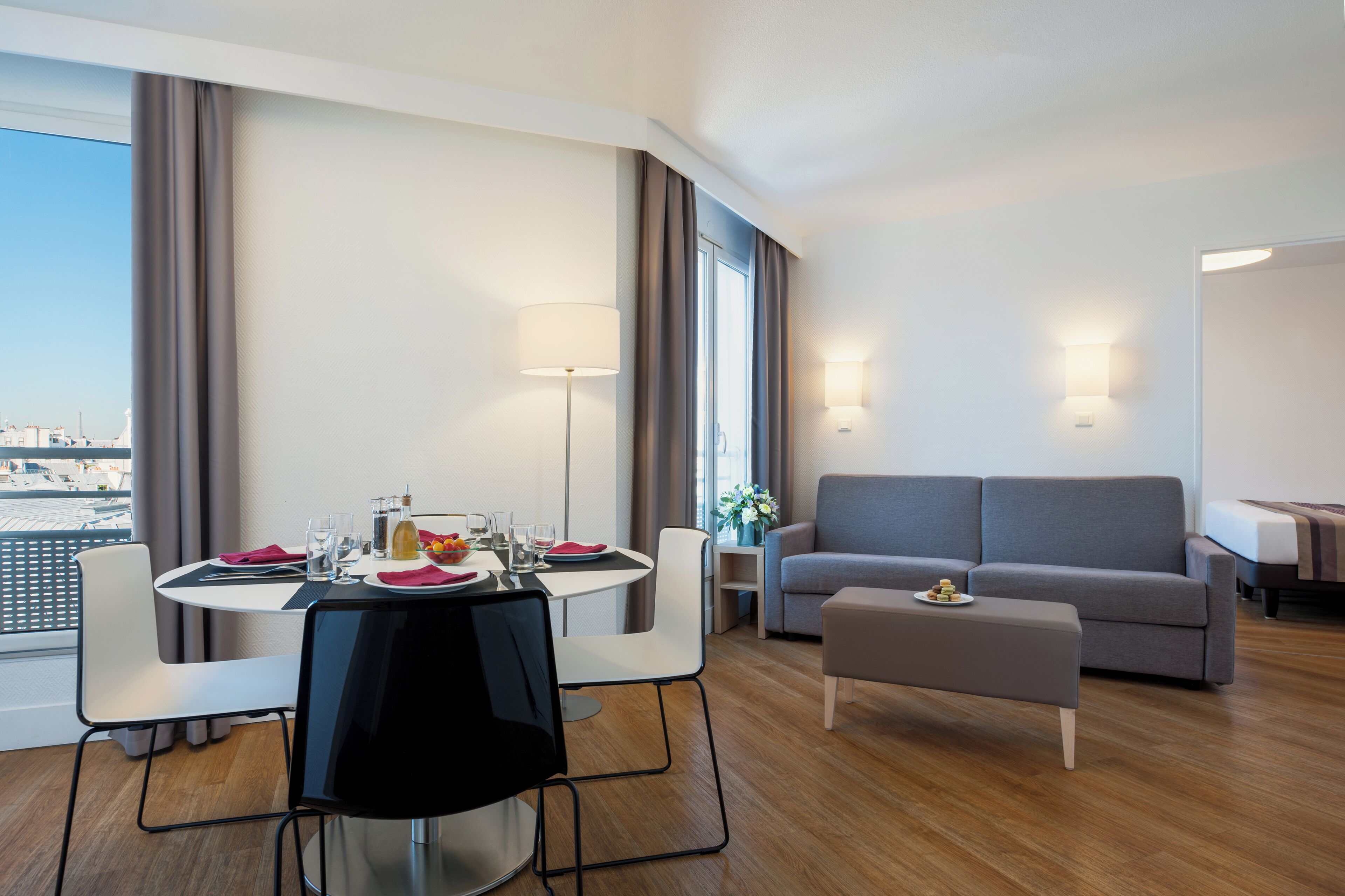A modern hotel room with a dining area, a sofa, and a view of the city.