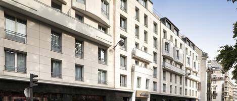 Un hotel de varios pisos con una fachada moderna, ventanas grandes y una entrada a nivel de calle con escaparate visible.