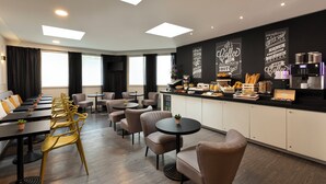 Una camera d'albergo moderna con zona pranzo, angolo caffè e un'ampia finestra che lascia entrare luce naturale.