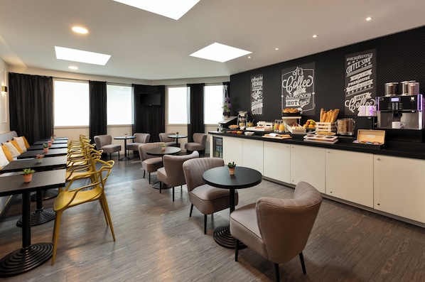 Una habitación de hotel moderna con zona de comedor, estación de café y un amplio ventanal que proporciona luz natural.