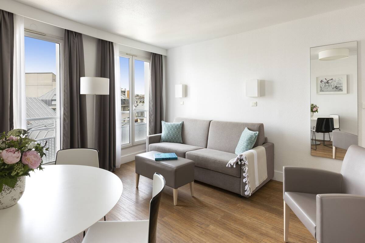 Una sala de estar moderna con sofá, sillas, una mesa de centro y una mesa de comedor con un jarrón de flores.