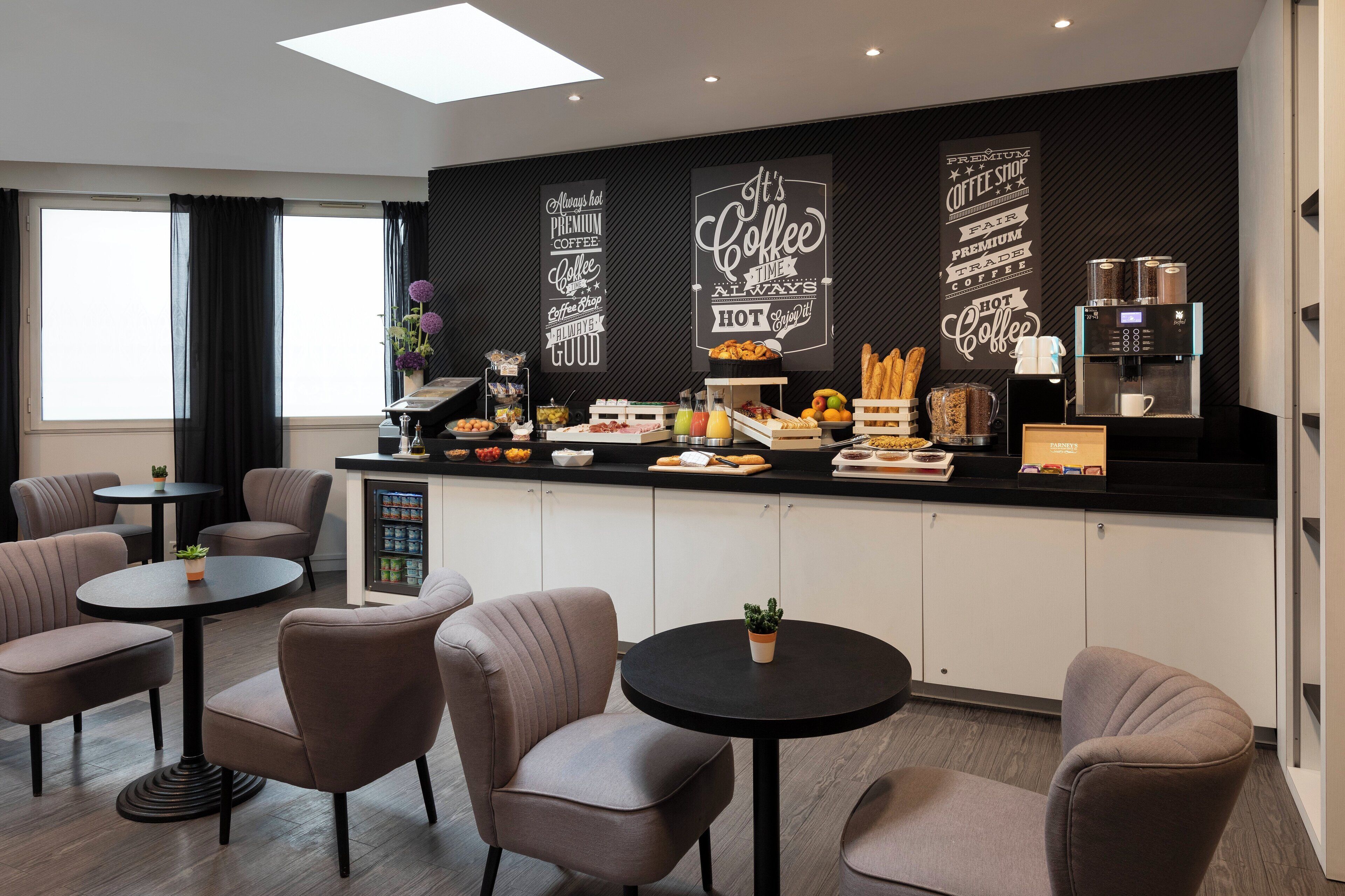 A modern coffee shop with a black counter, coffee machines, and a variety of food and drink options. There are several round tables and chairs for customers.