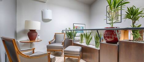 A modern living room with a sofa, armchairs, a small table with a lamp, and a decorative plant arrangement.