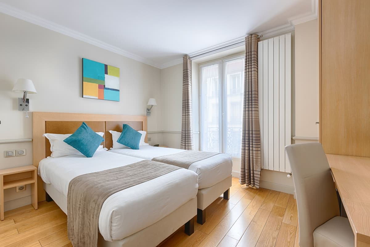 Ett hotellrum med två sängar, ett skrivbord och ett fönster med gardiner.
