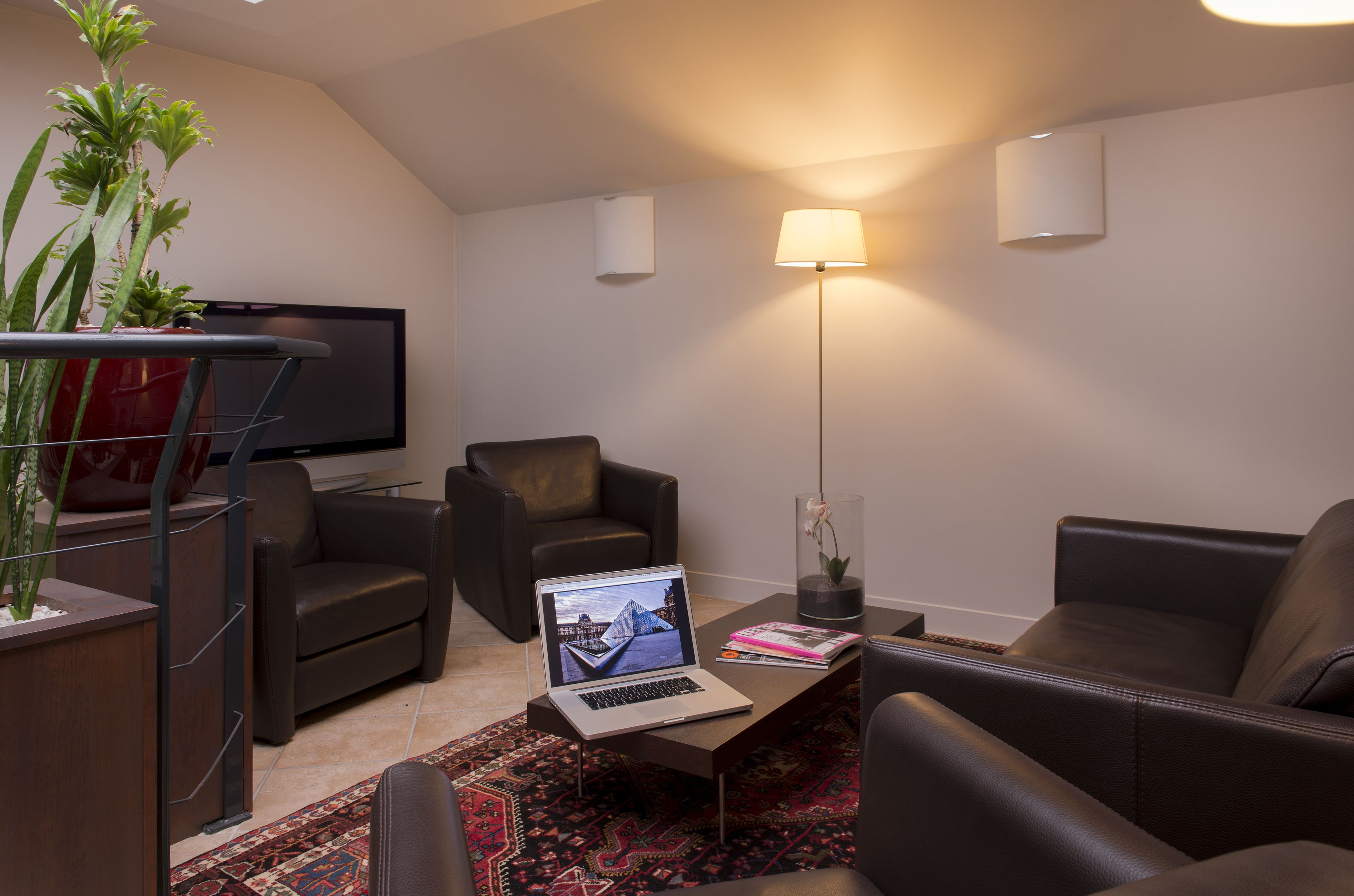 A modern living room with a laptop on a coffee table, two sofas, a TV, and a floor lamp.