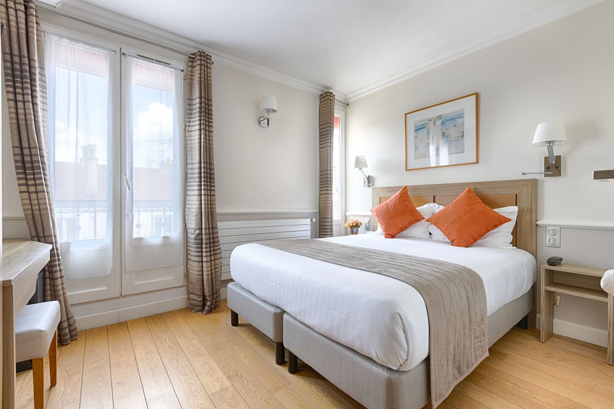 Ett hotellrum med en stor säng, en bänk, ett skrivbord och utsikt över staden genom fönstret.