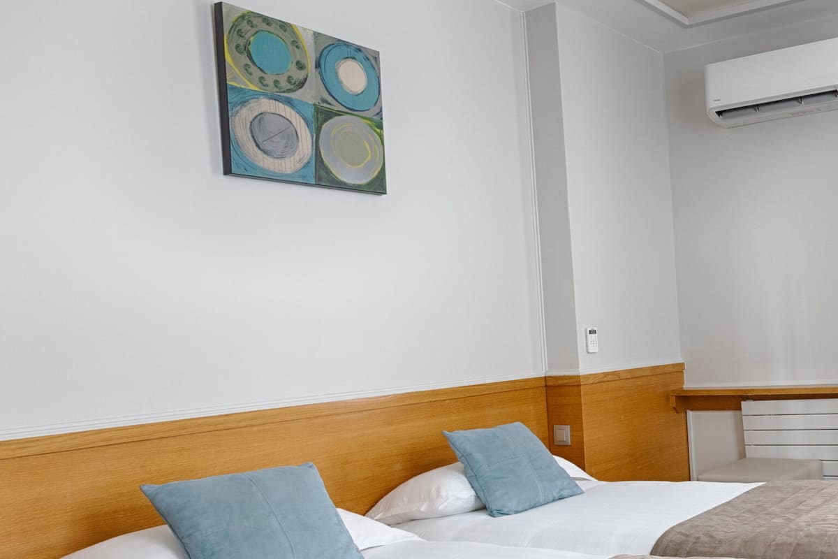 Ett hotellrum med två sängar, båda med vita lakan och blå kuddar. Det finns en träpanel bakom sängarna, en beige pläd och en tavla på väggen.