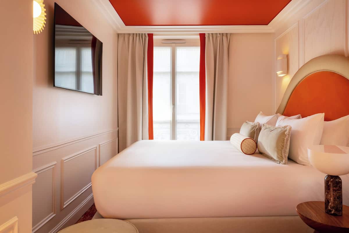 A hotel room with a large bed, a flat-screen TV mounted on the wall, and a window with curtains.