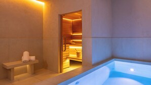 Et moderne spa-rum med et opvarmet stenbadekar, en bænk med håndklæder og et træsvedsauna-område.