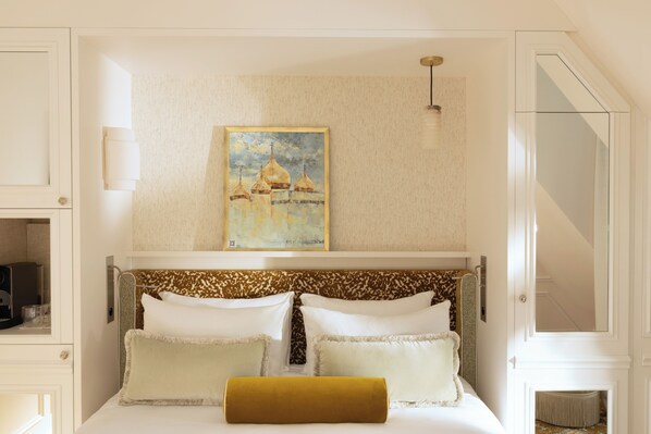 A neatly arranged bedroom with a bed, pillows, a headboard, a painting, and a light fixture.