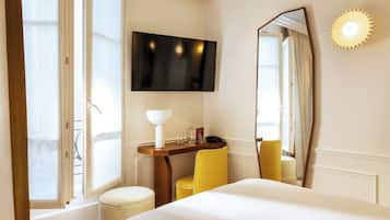 A hotel room with a bed, a desk with a lamp, a chair, a TV, and a large mirror.