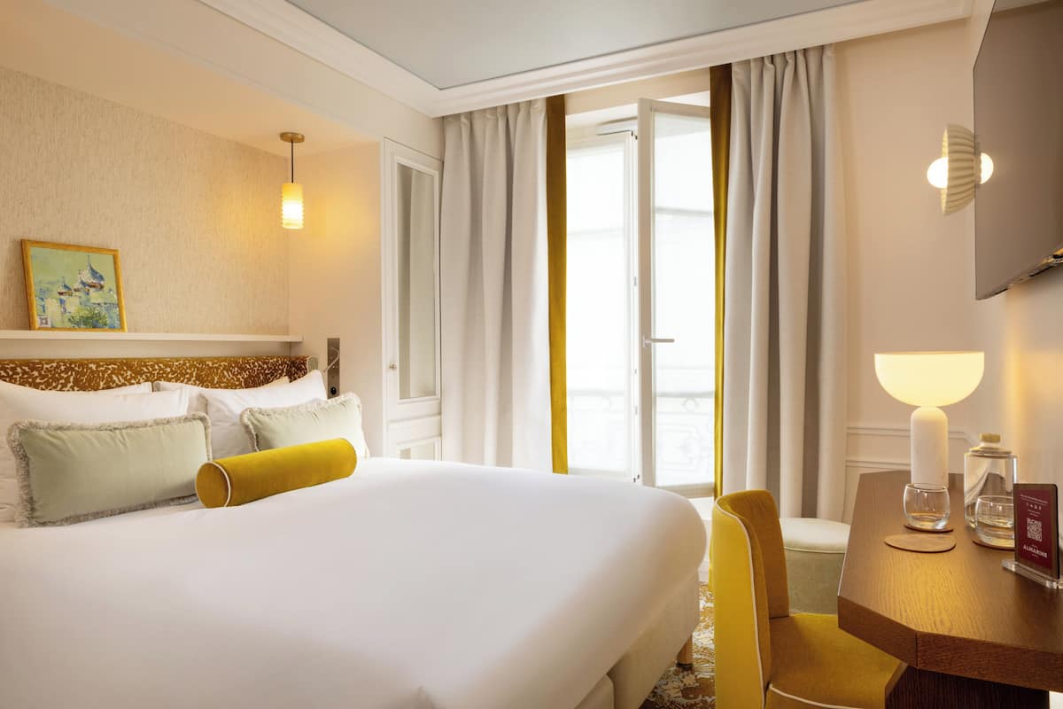 A hotel room with a large bed, a desk with a lamp, and a view of the outdoors through a window.