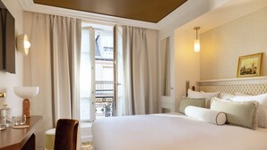 Et hotelværelse med en stor seng, et skrivebord med stol, et lille bord med glas og et lys, samt en balkon med gelænder.
