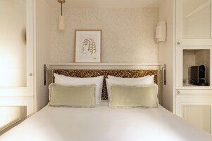 A neatly made bed with two pillows, a headboard with a leopard print pattern, a framed artwork on the wall, and a bedside table with a lamp.