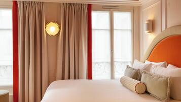 A hotel room with a large bed, beige curtains, a sun-shaped light fixture, and a wall-mounted light.