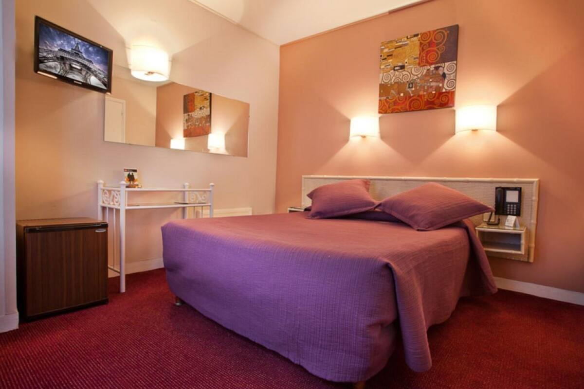A bedroom with a bed, a bedside table, a lamp, a TV, and a mirror.
