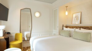 Et hotelværelse med en stor seng, en gul stol, et spejl og en lampe på væggen.