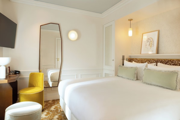 Una habitación de hotel con una cama grande, una silla amarilla, un espejo y una lámpara fijada a la pared.