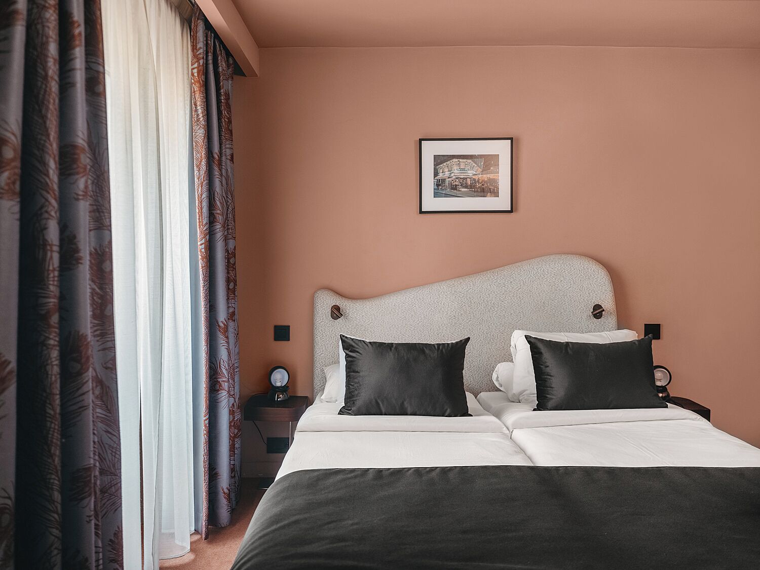 A neatly made bed with two black pillows, a white comforter, and a headboard with a textured pattern. There is a framed picture on the wall above the bed.