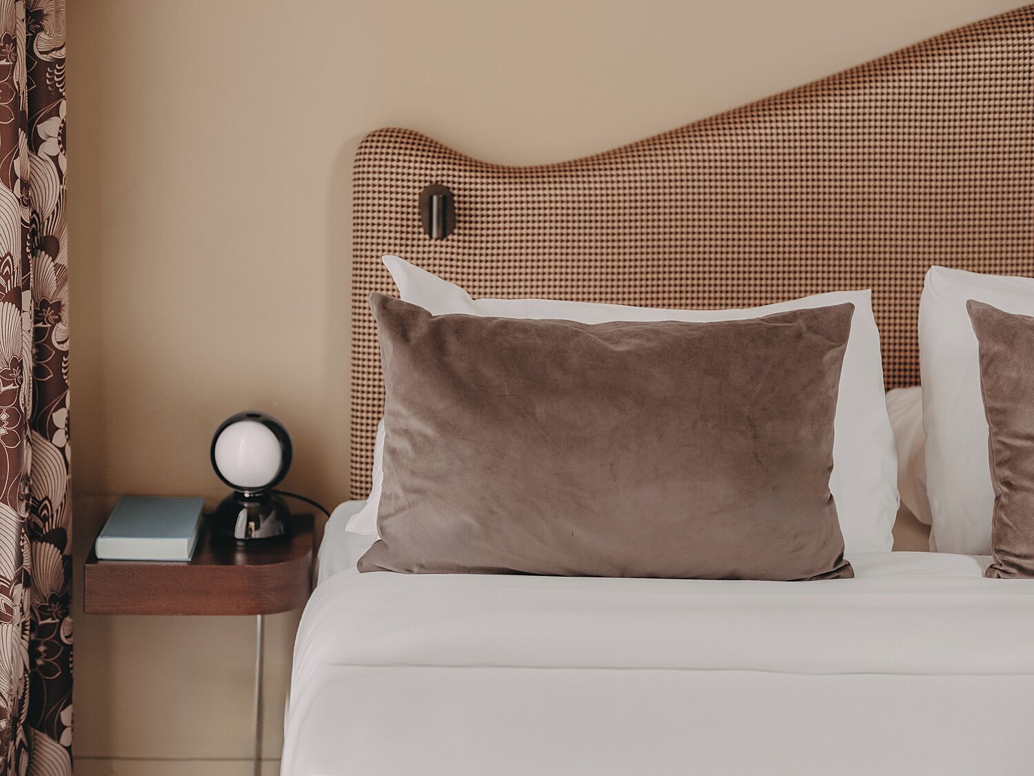 En pænt redt seng med to puder, et sengebord med en lampe og en ternet sengegavl.
