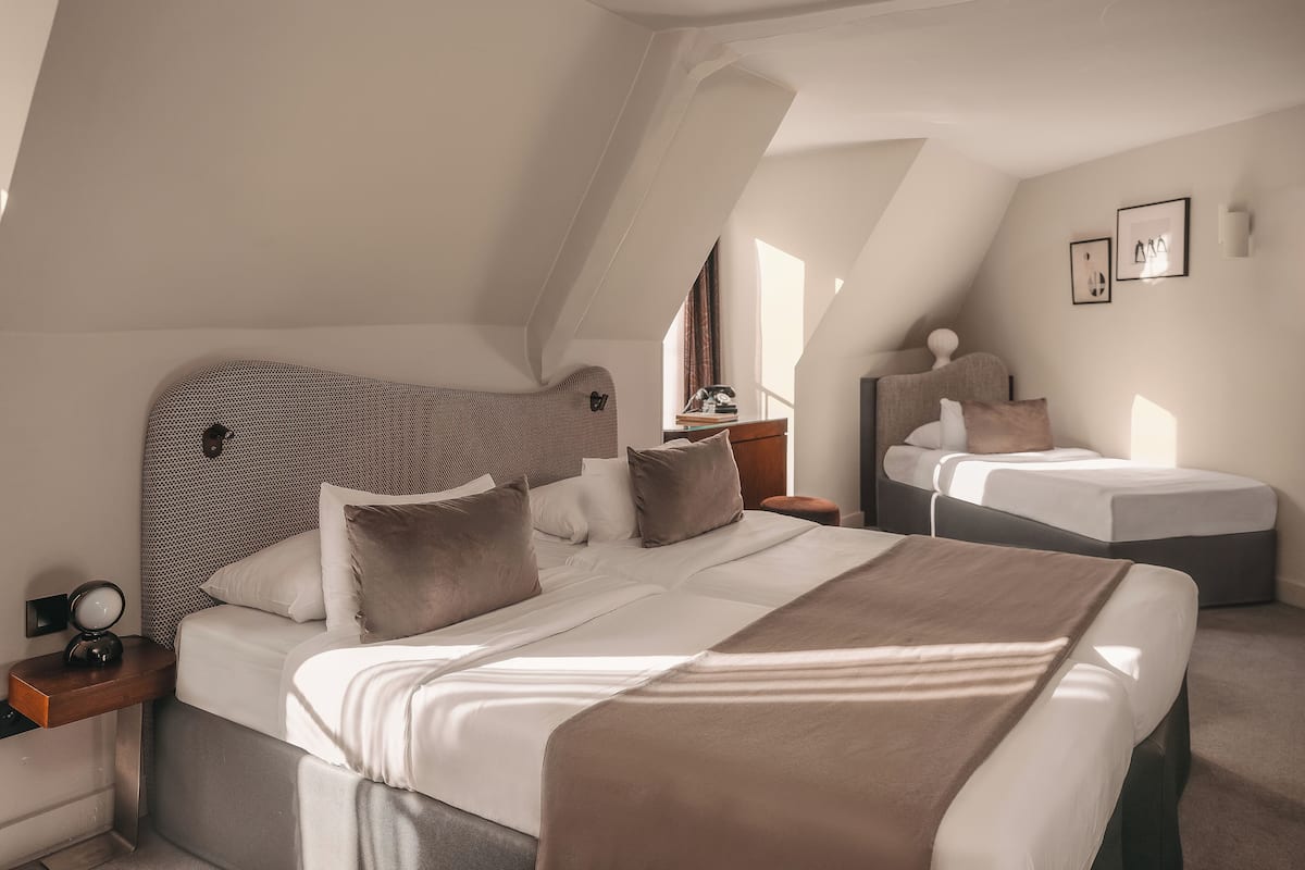 Un dormitorio moderno y bien iluminado con una cama grande, una cama más pequeña y un escritorio con lámpara.