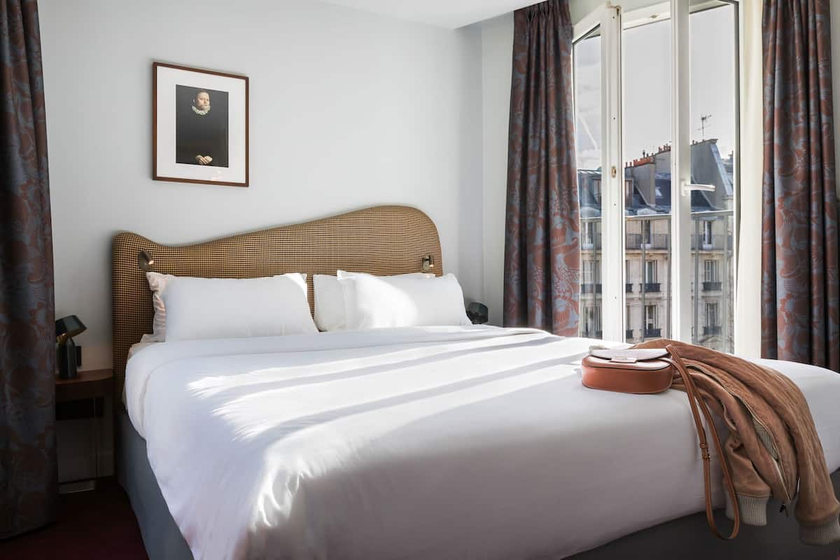 Habitación de hotel con una cama grande, un cuadro en la pared y vistas de edificios a través de la ventana.