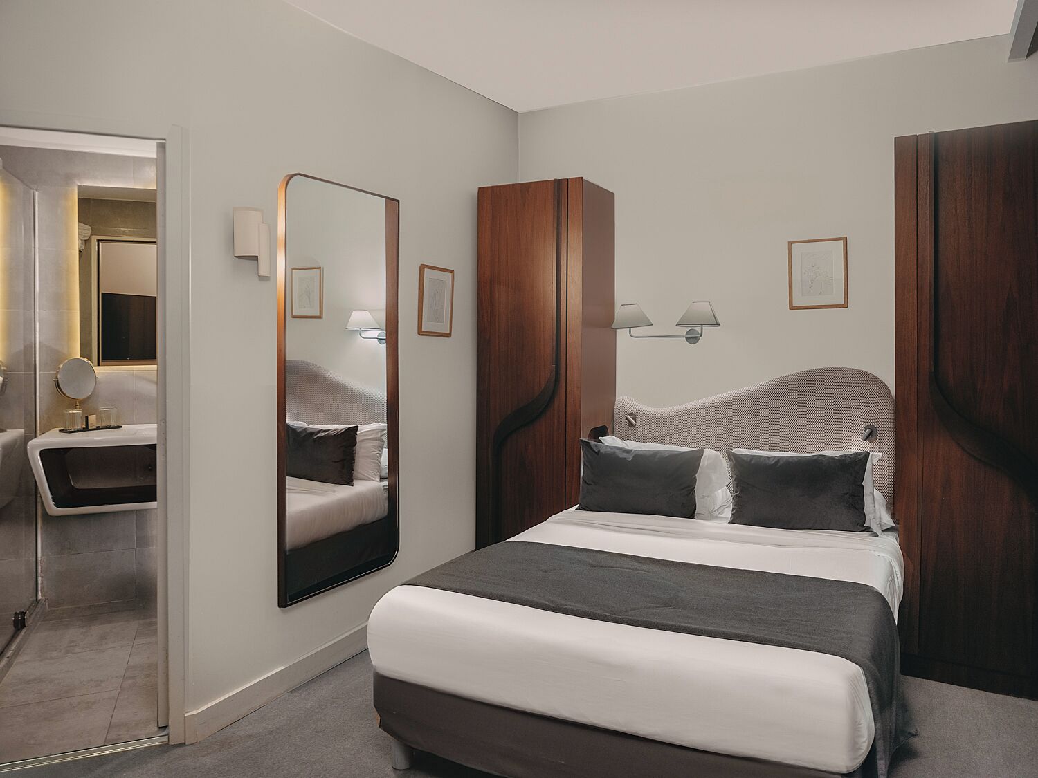 Una habitación de hotel moderna con una cama grande, un tocador con espejo y un armario de madera.