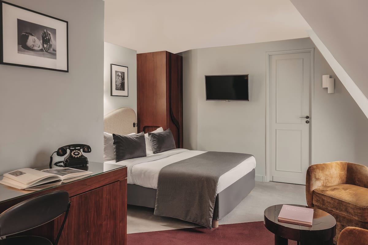 Una habitación de hotel moderna con una cama, un escritorio con un teléfono, un televisor y una silla.